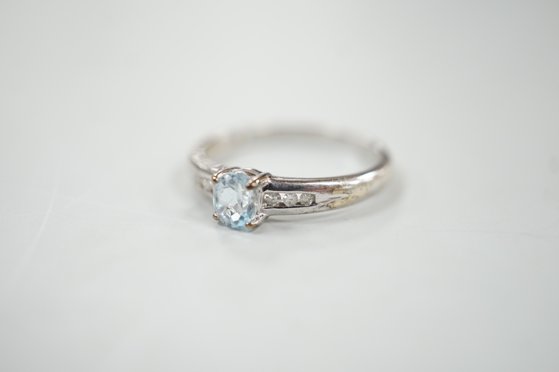 A modern 9ct white gold and oval cut blue topaz ring, with diamond chip set shoulders, size N, gross weight 2 grams.